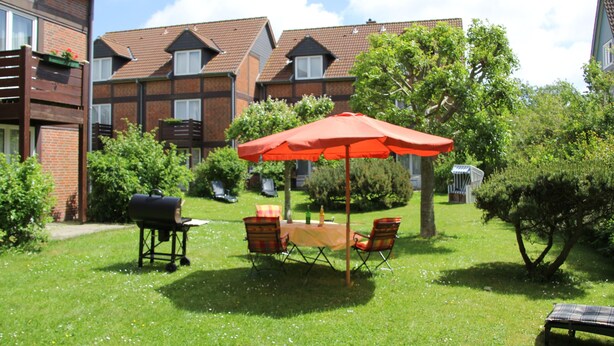 A backyard with a barbecue grill, a table with chairs, and an umbrella. - Apartment 'Atlanta 202' with Private Terrace, Private Garden and Wi-Fi (Pellworm)