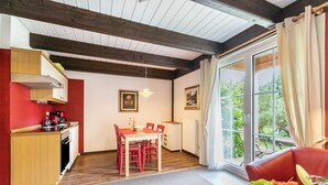 A room with a dining table, chairs, a red sofa, a kitchen area, and a large window with curtains. - Apartment 'Atlanta 202' with Private Terrace, Private Garden and Wi-Fi (Pellworm)