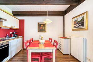 Une cuisine avec une table à manger, des chaises, un luminaire suspendu, un tableau encadré et un radiateur.