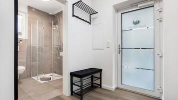 A modern bathroom with a glass shower enclosure, a bench with storage, and a frosted glass door with a logo.