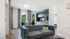 Una sala moderna con un sofá verde, una mesa de comedor y una cocina al fondo.