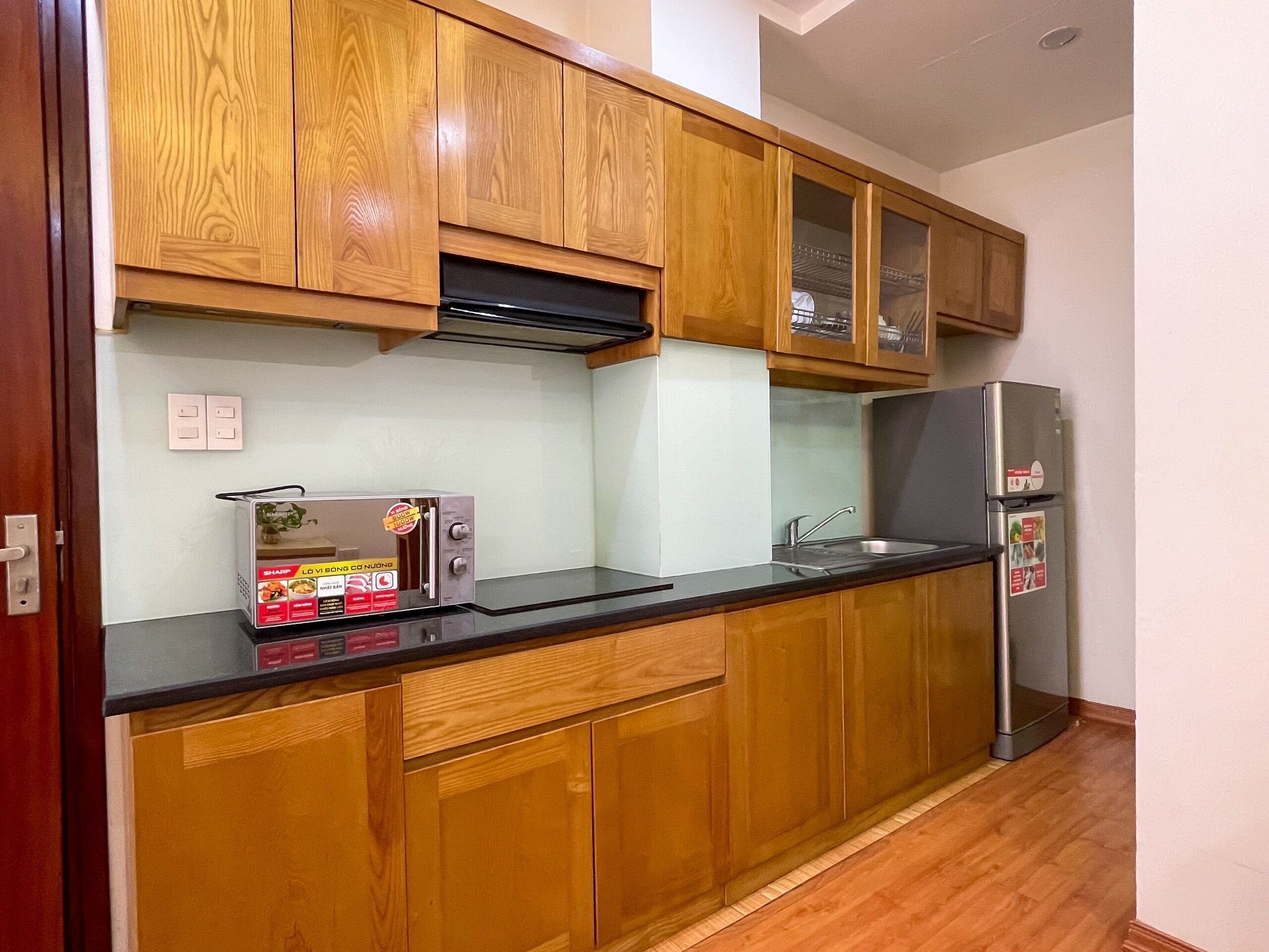 A kitchen with wooden cabinets, a black countertop, a stainless steel refrigerator, and a built-in oven.