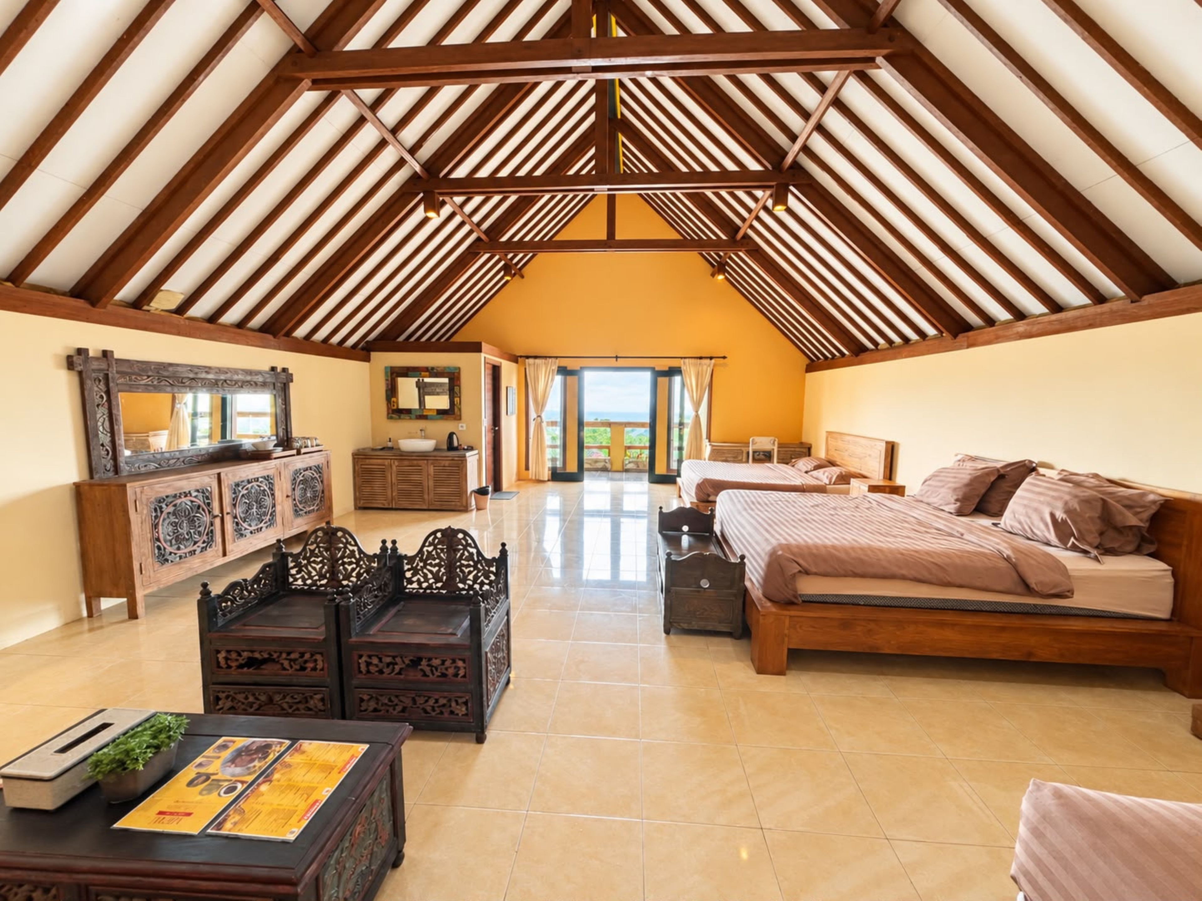 A spacious room with a high ceiling, a large bed, a wooden cabinet, and a dining table.