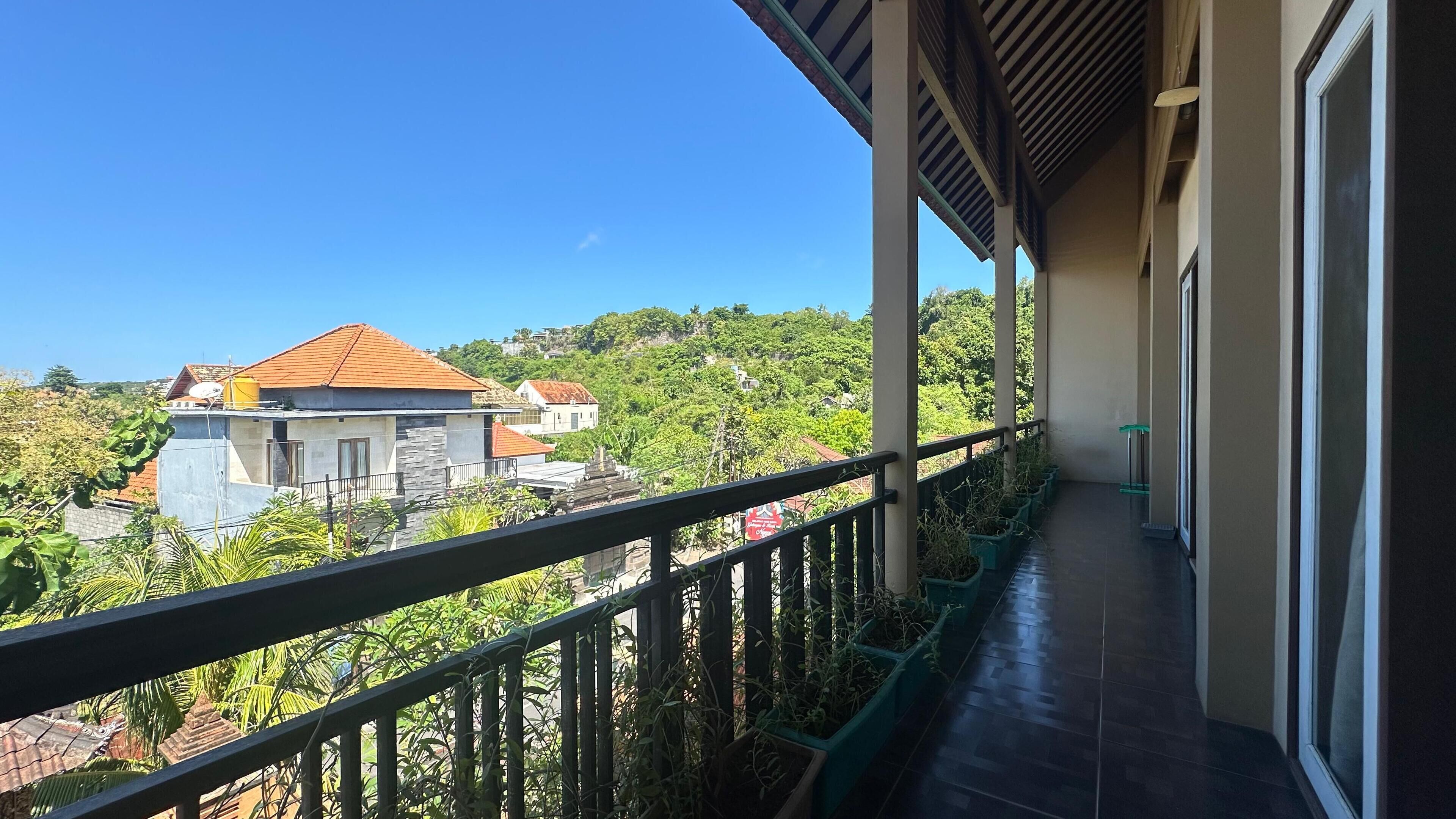 A balcony with a view of a hillside, a railing, and potted plants.