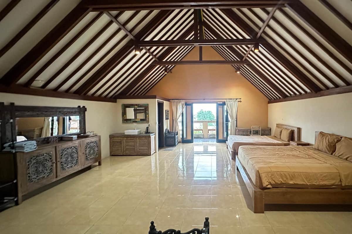 A spacious bedroom with a high ceiling, a large bed, a wooden dresser, and a bathroom with a sink and mirror.