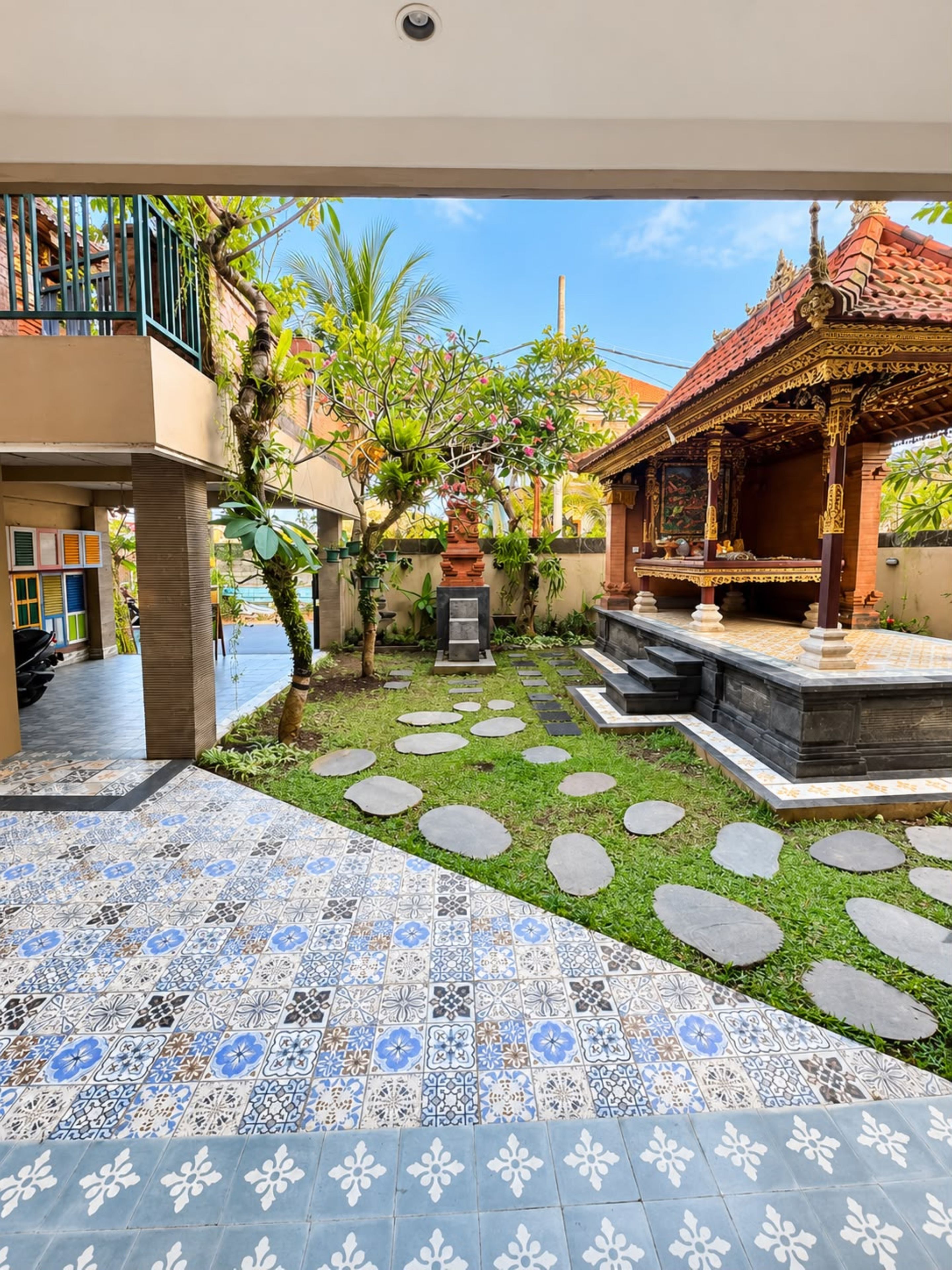 Un patio con piso de baldosas, una pequeña área ajardinada con piedras y una estructura tradicional con detalles ornamentales.