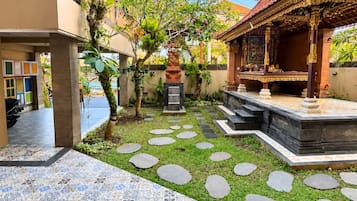Un patio con piso de baldosas, una pequeña área ajardinada con piedras y una estructura tradicional con detalles ornamentales.