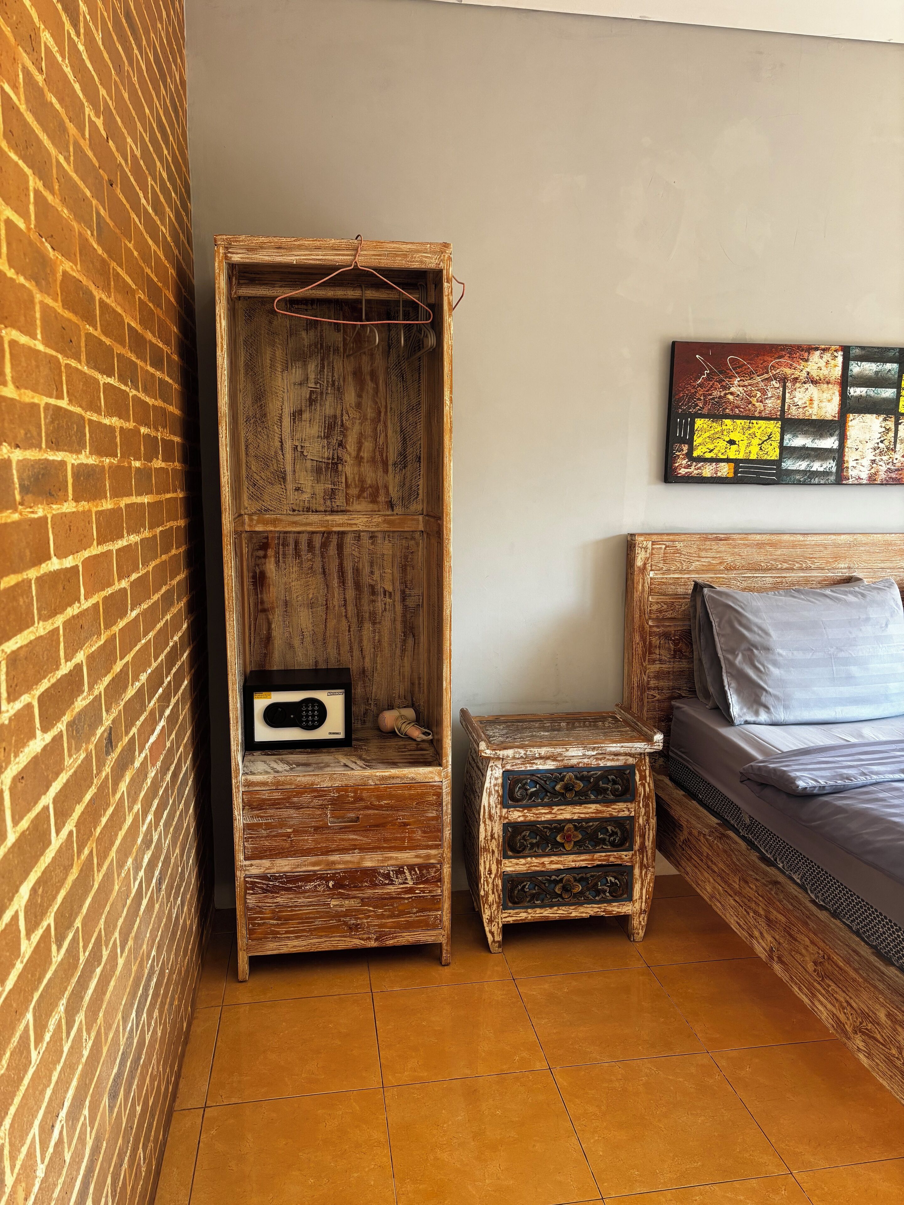 Un dormitorio con una cama, un armario de madera, un taburete pequeño y una obra de arte en la pared.