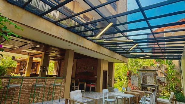An outdoor patio with wooden furniture, a glass ceiling, and a view of a building in the background.
