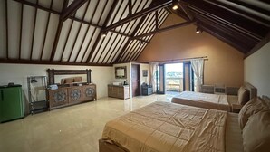 A spacious bedroom with a high ceiling, a large bed, a dresser, and a view of the outdoors.