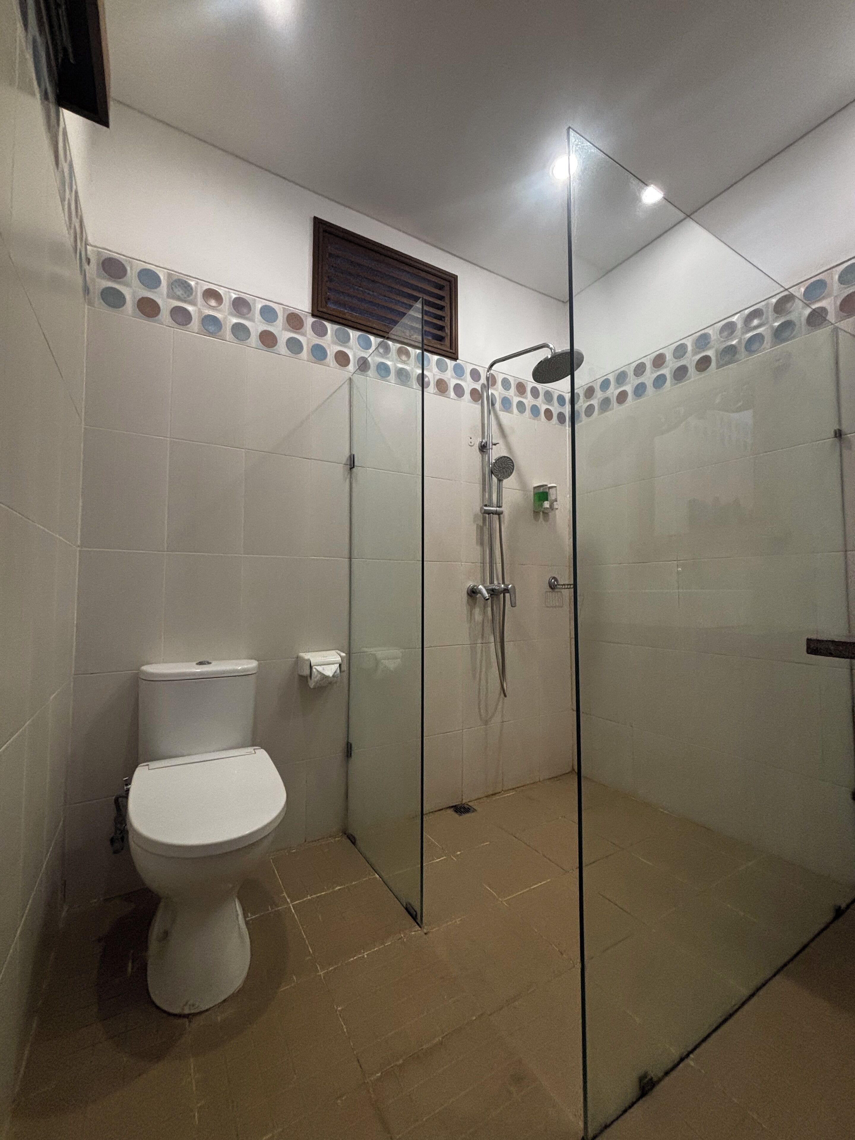 A bathroom with a toilet, a glass-enclosed shower, and tiled walls.