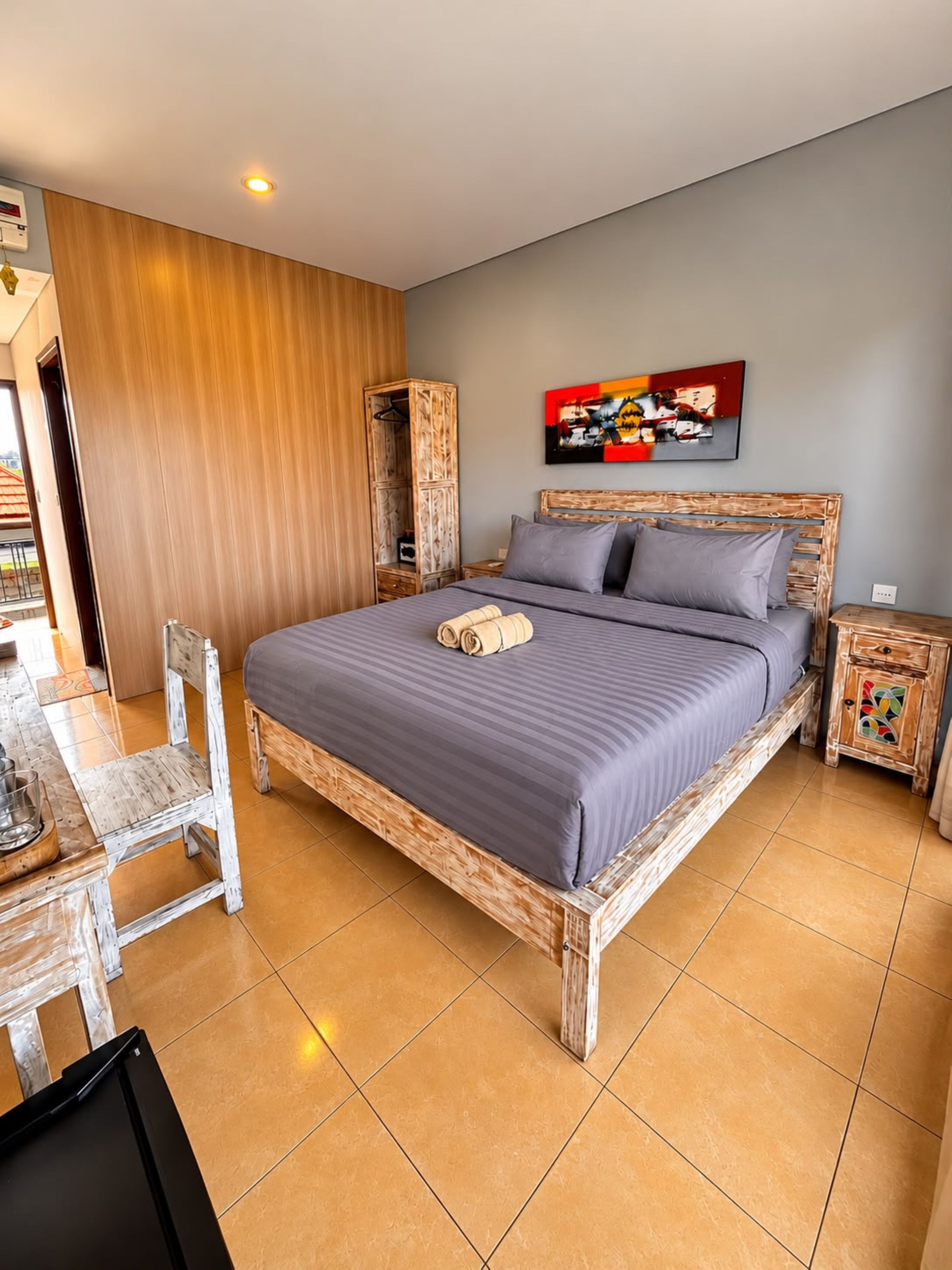A bedroom with a wooden bed frame, a grey mattress, a wooden nightstand, a wooden wardrobe, and a painting on the wall.