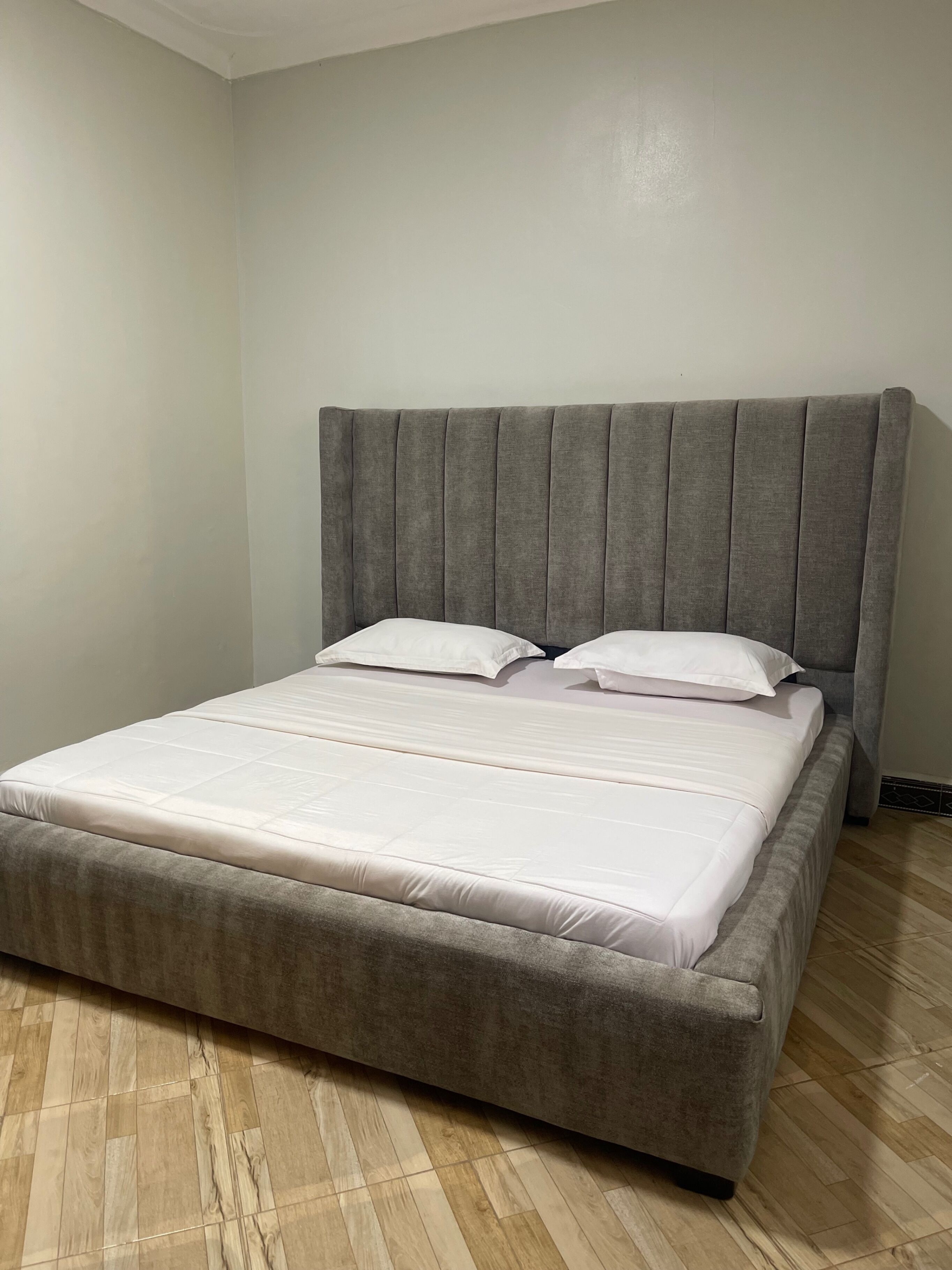 A bed with a grey upholstered headboard and white bedding in a room with wooden flooring.