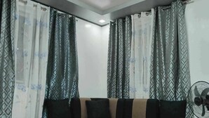 A corner sofa with black cushions, a tiled floor, and patterned curtains. - 3G's & C Calapan Transient House (Calapan)