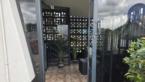 Une porte vitrée donne accès à un patio dont le sol est recouvert de carreaux de pierre, avec un espace détente extérieur doté de mobilier noir et une structure décorative en treillis noir.
