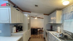 A narrow kitchen with white cabinets, a wooden countertop, and a central island.