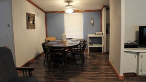 A dining area with a round table, chairs, a ceiling fan, and a window with blinds.