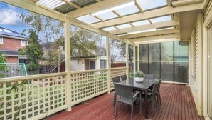 Eine überdachte Terrasse im Freien mit Tisch und Stühlen, eine Holzterrasse und Blick auf Nachbarhäuser.