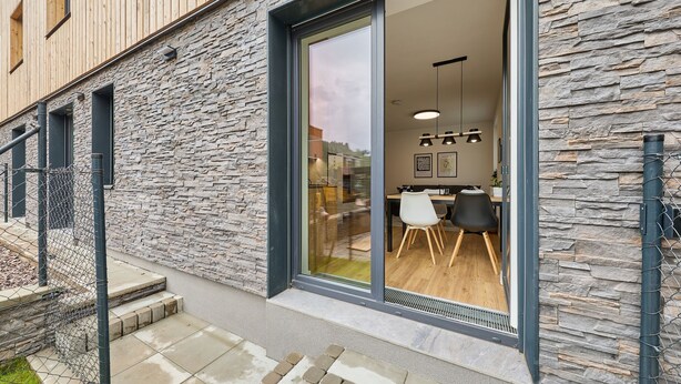 En moderne bygning med stenfassade og store skydedøre, der fører til et spiseområde med et bord og stole.