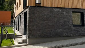 En moderne bygning med en træfacade, en stensokkel og et belagt indgangsparti.