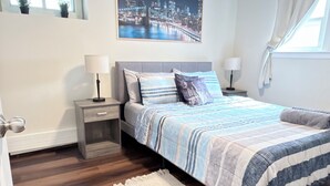 A bedroom with a bed, nightstands, a window, a painting, and a wooden floor. - Apartment with excellent location, a few minutes from Manhattan New York (Jersey City)