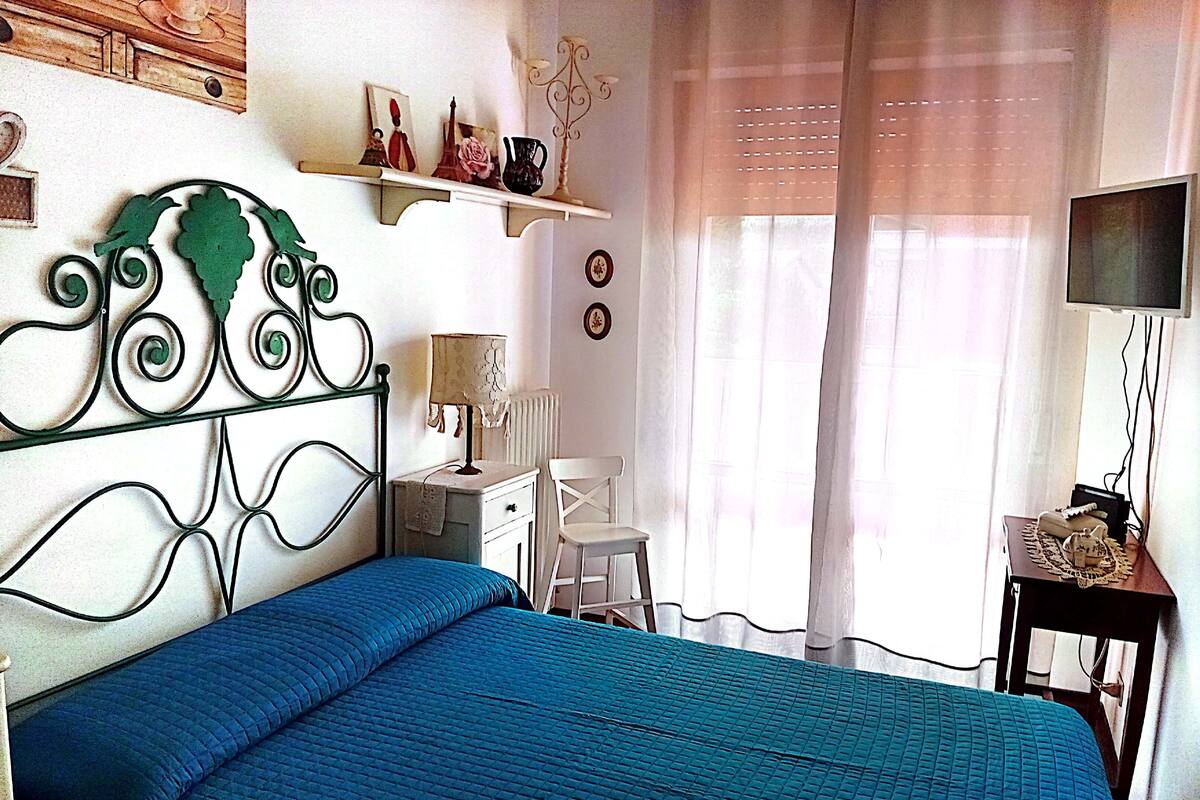Een slaapkamer met een bed, een bureau, een stoel, een televisie en een raam met gordijnen.