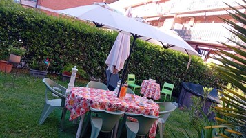 Un patio al aire libre con una mesa, sillas, un paraguas blanco y una siega en el fondo.