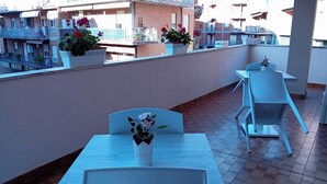 A rooftop terrace with outdoor seating, potted plants, and a view of neighboring buildings. - Giardino del Sole (Ascoli Piceno)