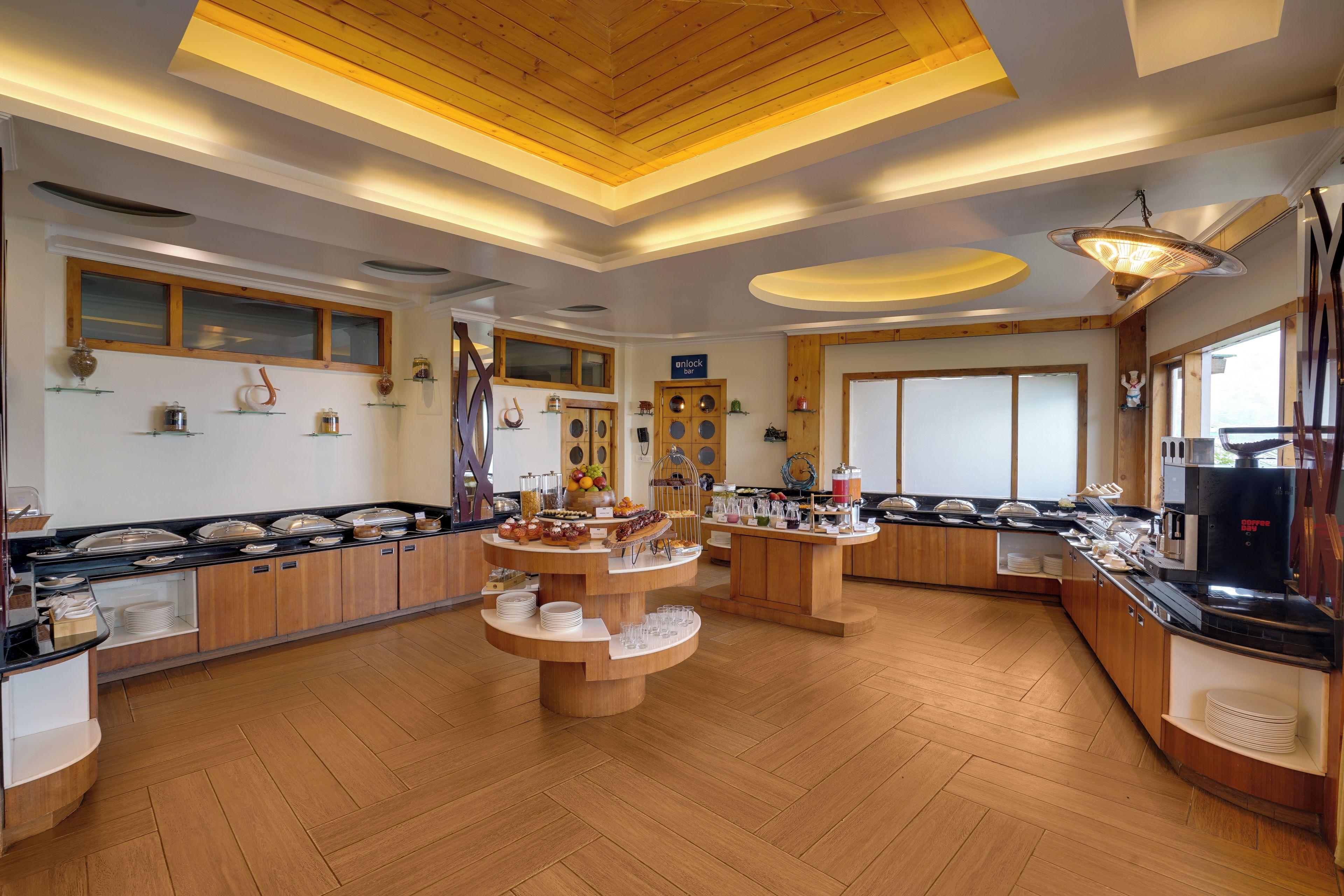 A modern breakfast area with wooden flooring, a coffee machine, and a variety of breakfast items on display.
