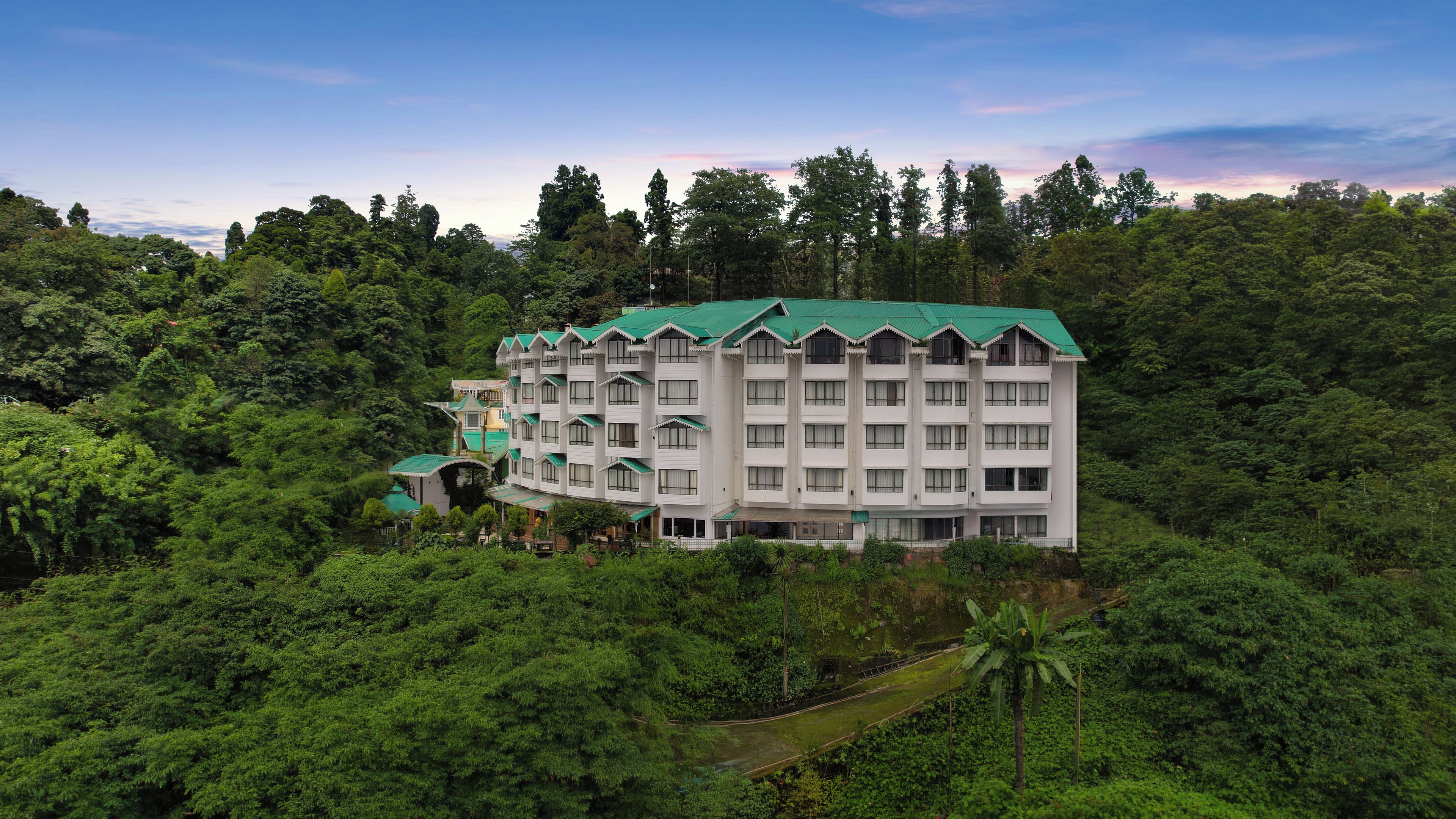A multi-story hotel with a green roof, surrounded by dense forest.