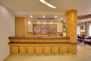 A reception area with a wooden reception desk, a marble wall with decorative panels, and a seating area with a sofa. - KEYS PRIMA BY LEMON TREE HOTELS  (Darjeeling)