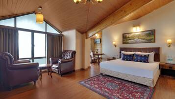 A hotel room with a large bed, a desk, a chair, and a view of the outdoors through the window.