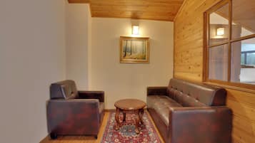A room with a wooden ceiling, a painting on the wall, a sofa, two armchairs, and a small round table.