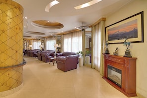 A spacious lobby with leather sofas, a wooden column, a fireplace, and a large window with curtains. - KEYS PRIMA BY LEMON TREE HOTELS (Darjeeling)