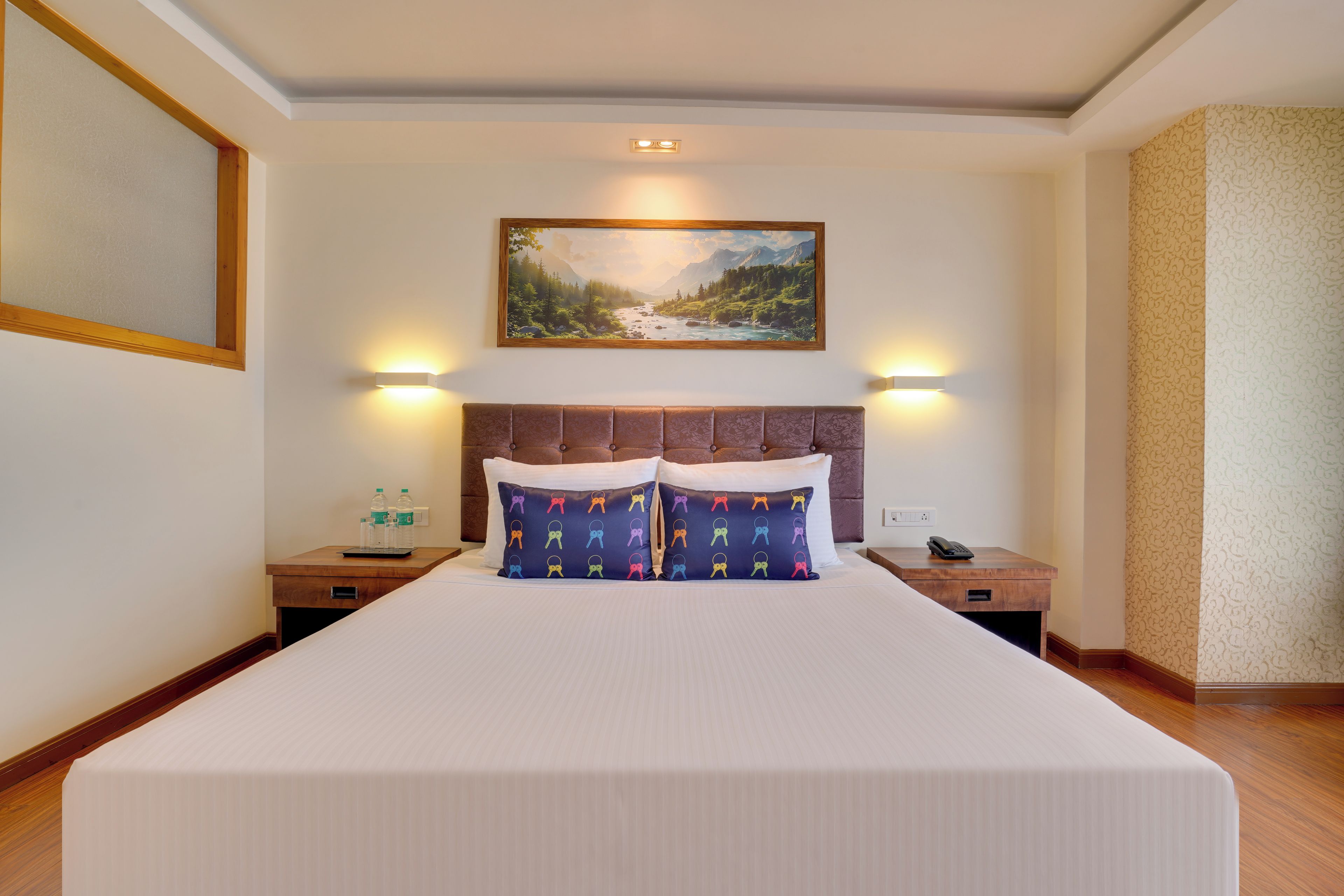 Habitación de hotel con una cama grande, cabecera, dos mesitas de noche, un cuadro en la pared y un teléfono sobre una de ellas.