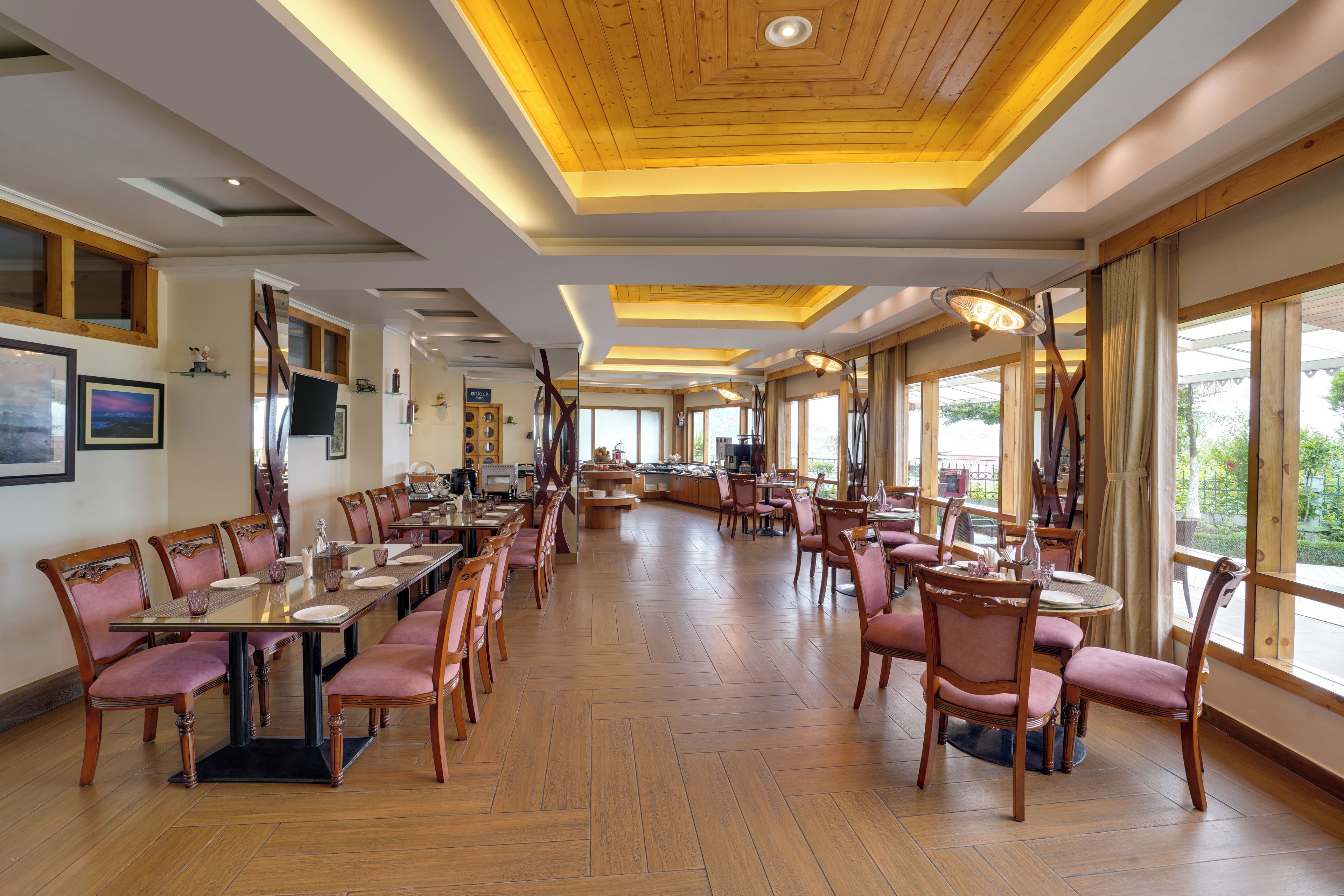 A spacious dining area with multiple tables and chairs, wooden flooring, and large windows offering views.