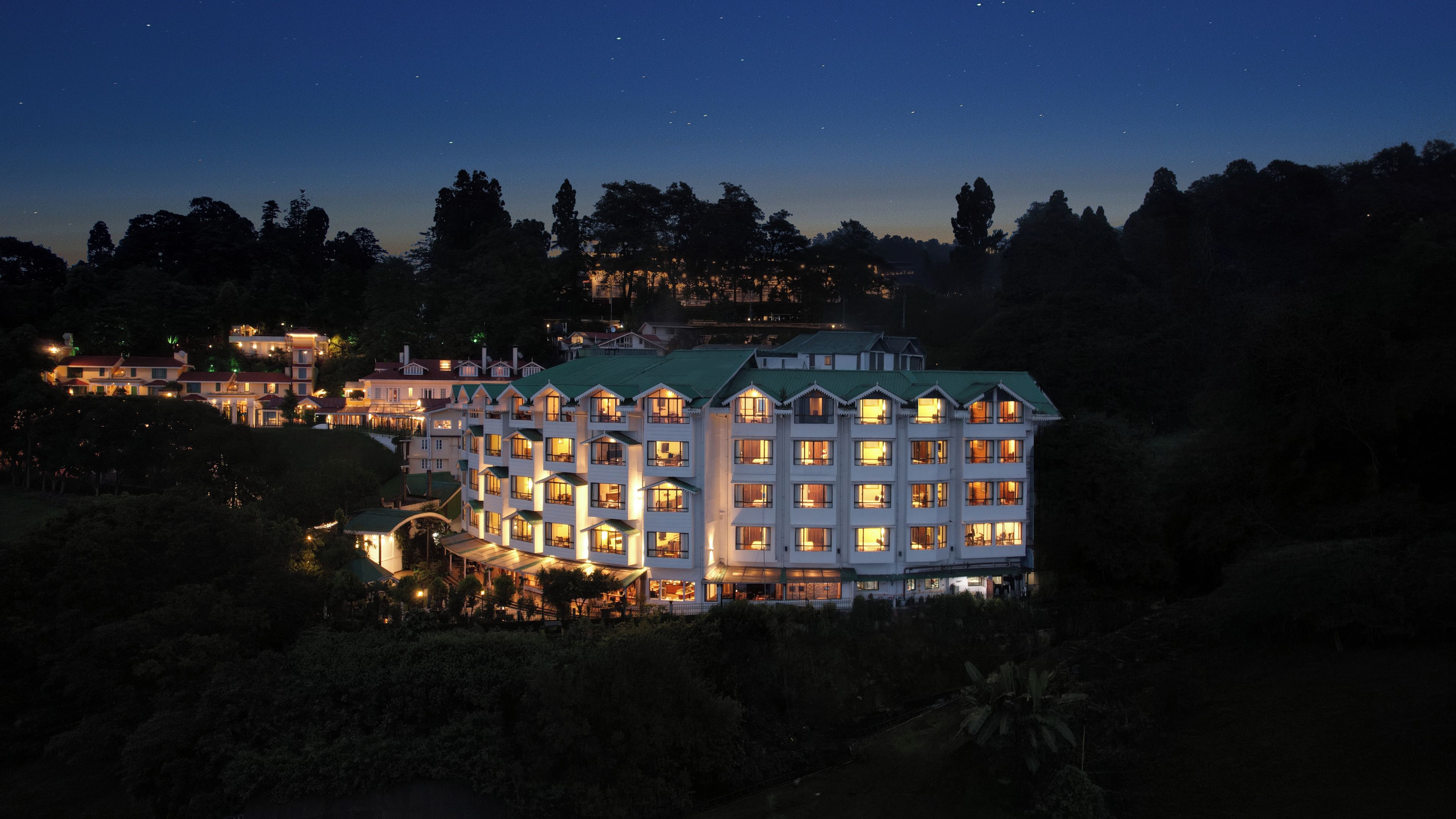 Un hotel de varios pisos con ventanas iluminadas, rodeado de árboles y un cielo nocturno despejado.