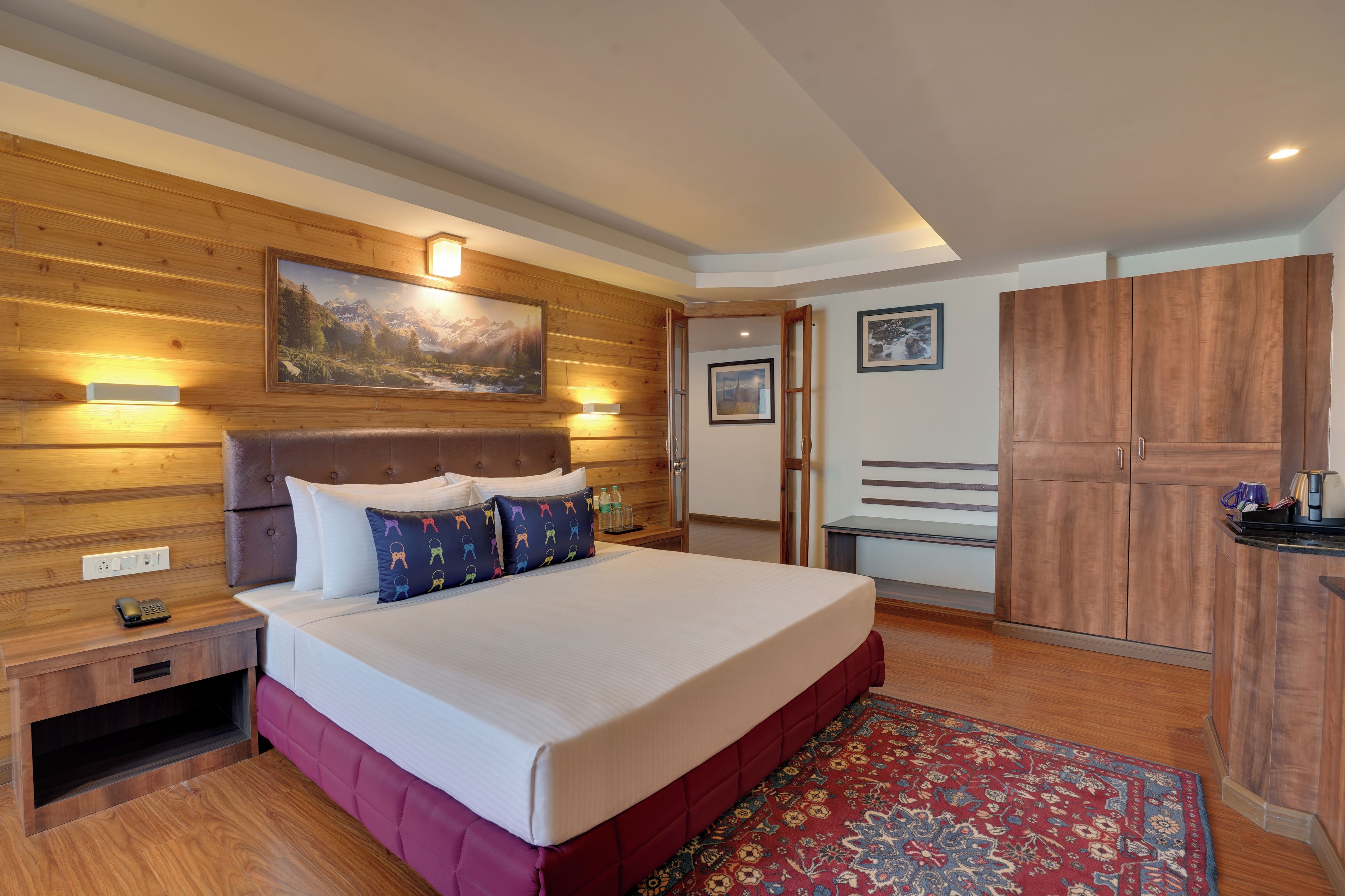 Habitación de hotel con cabecera de madera, cama grande con ropa de cama blanca, pared de acento roja, armario de madera y un cuadro sobre la cama.