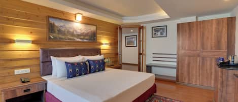 A hotel room with a wooden headboard, a large bed with white bedding, a red accent wall, a wooden wardrobe, and a painting above the bed.