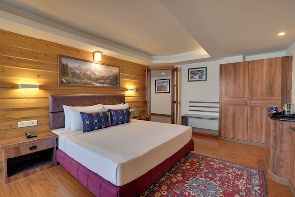 A hotel room with a wooden headboard, a large bed with white bedding, a red accent wall, a wooden wardrobe, and a painting above the bed. - KEYS PRIMA BY LEMON TREE HOTELS (Darjeeling)