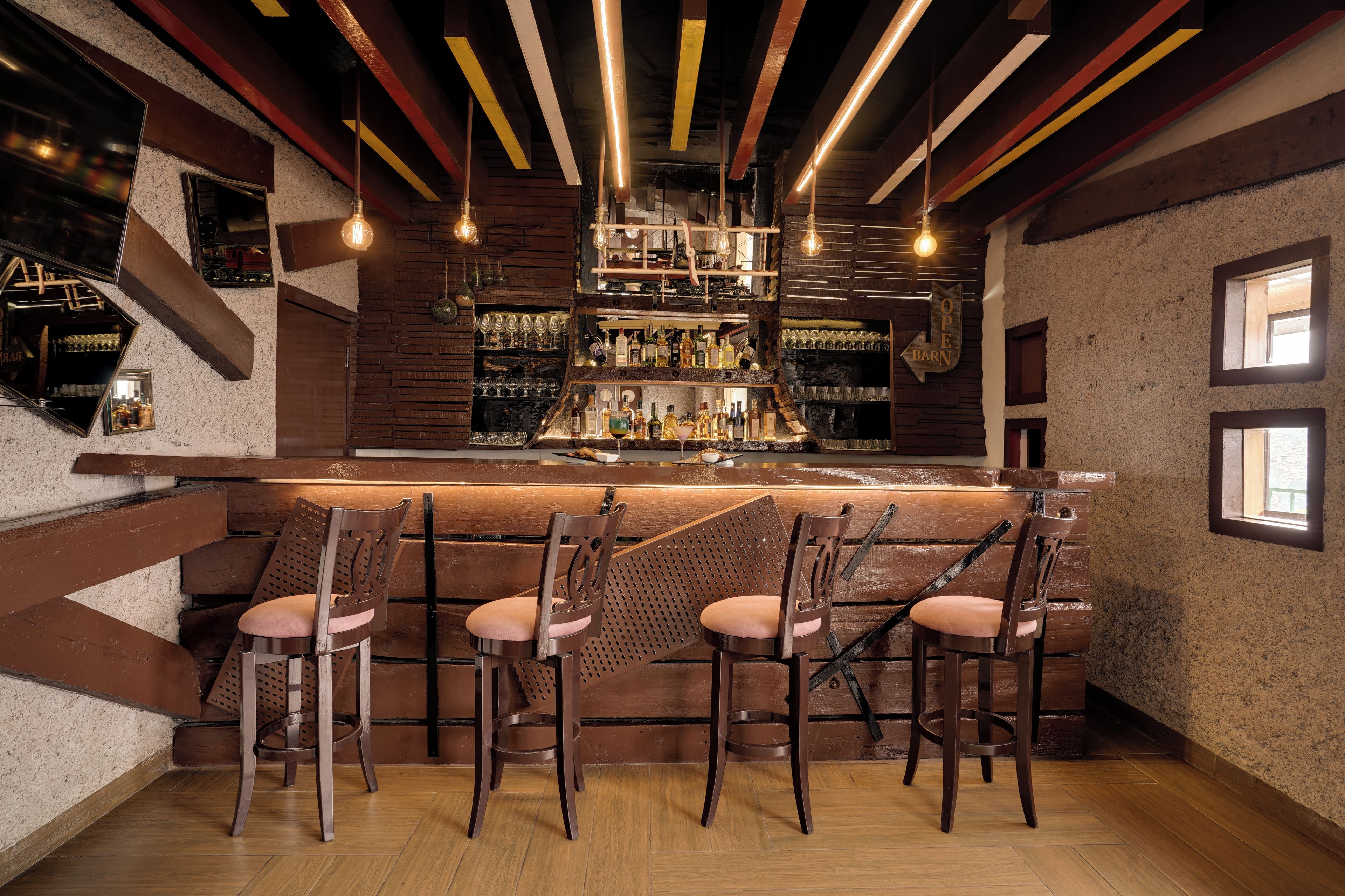 A bar area with wooden bar stools, a bar counter stocked with bottles, and a rustic ceiling with exposed beams and hanging lights.