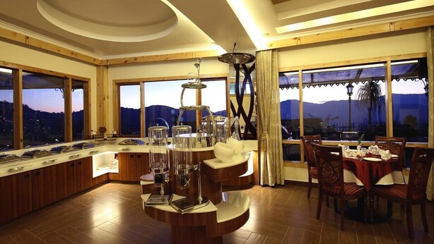 Une cuisine moderne dotée d’un îlot central, de grandes fenêtres et d’un coin repas avec une table dressée pour quatre personnes.