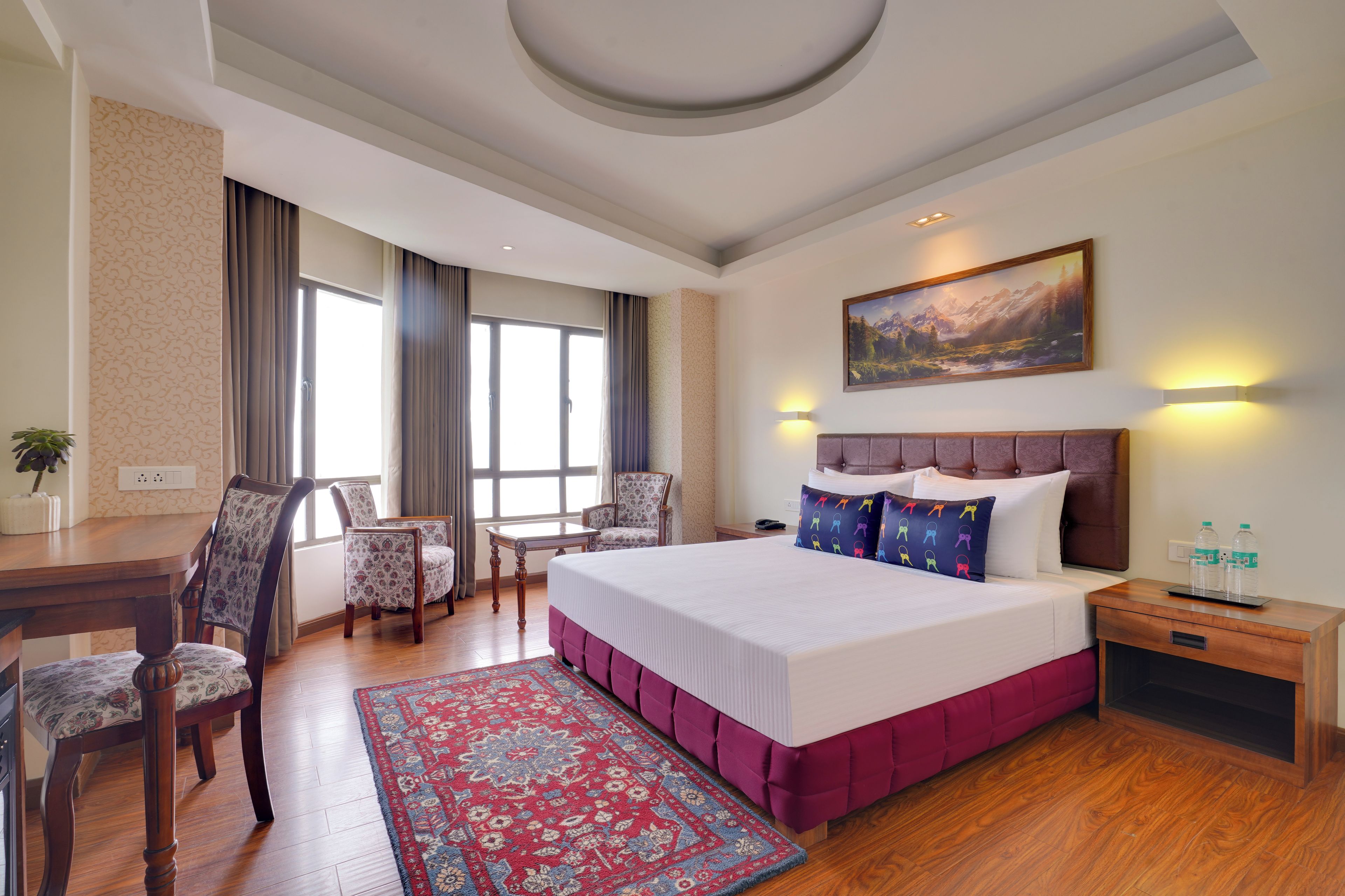 Una camera d'albergo con un letto grande, una scrivania, due sedie, un tappeto e un quadro appeso al muro.