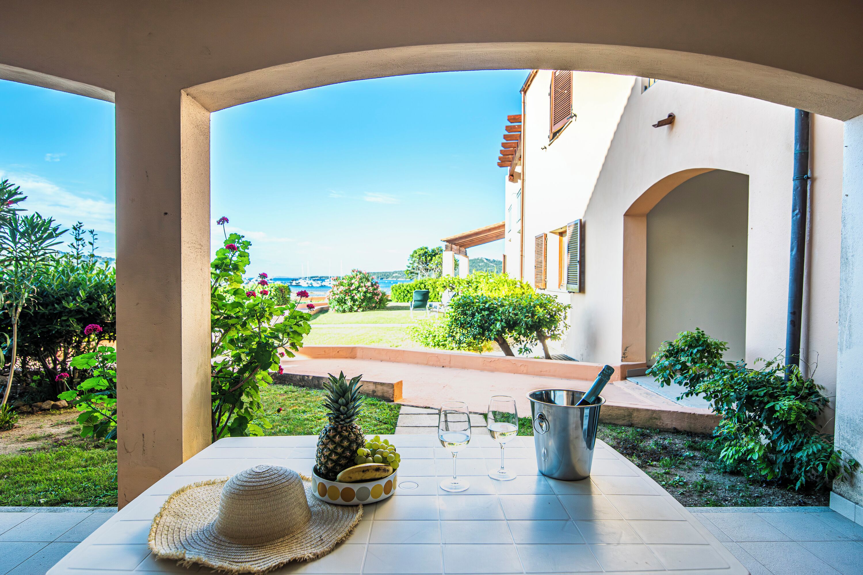 A patio with a table set for two, featuring a pineapple, grapes, a hat, and a wine glass.