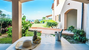 Eine Terrasse mit einem Tisch, gedeckt für zwei Personen, mit einer Ananas, Trauben, einem Hut und einem Weinglas.