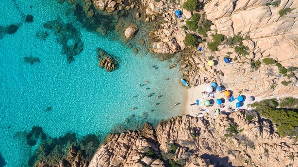 An aerial view of a rocky coastal area with clear turquoise water, a sandy beach, and scattered rocks. - Su Entu, Palau, Italy (Palau)