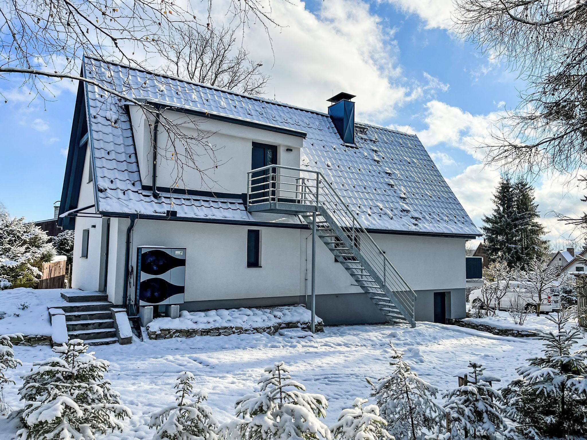 Ein modernes Haus mit einer Metalltreppe, die zu einem Balkon führt, umgeben von schneebedeckten Bäumen.