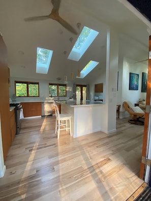 A modern kitchen with skylights, a dining area, and a living space with a chair and artwork.