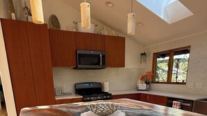 A modern kitchen with a large island, wooden cabinets, a microwave, and pendant lights.