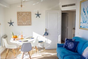 Een eethoek met een ronde tafel, witte stoelen en een blauwe bank met decoratieve kussens.